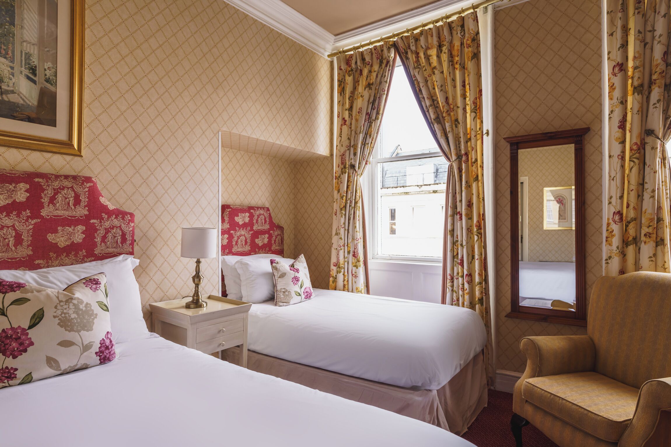 A hotel room with two beds, a nightstand, a chair, and a window with curtains.