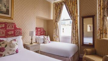 A hotel room with two beds, a nightstand, a chair, and a window with curtains.