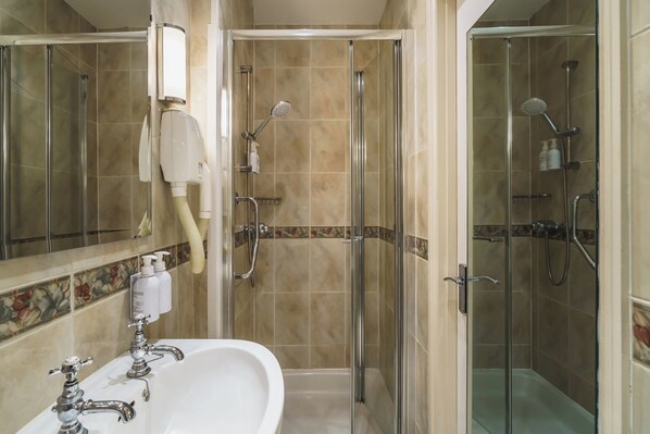 A bathroom with a glass-enclosed shower, a sink with a mirror, and toiletries on the wall.