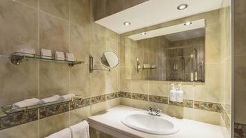 A modern bathroom with a large mirror, a glass shelf with toiletries, and a marble-tiled wall.