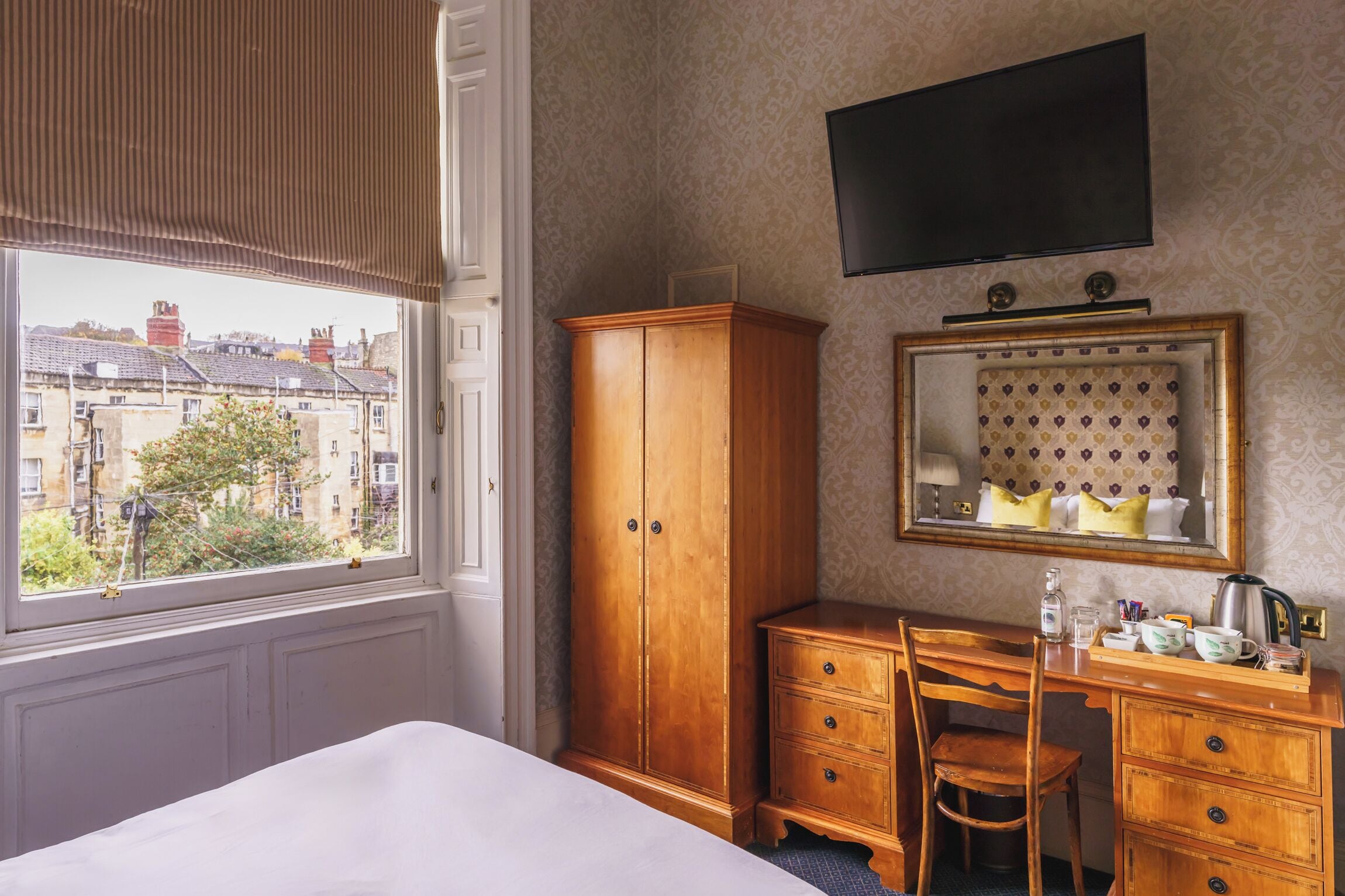 Ein Hotelzimmer mit großem Kleiderschrank, Schreibtisch mit Stuhl, Spiegel und Wandfernseher.
