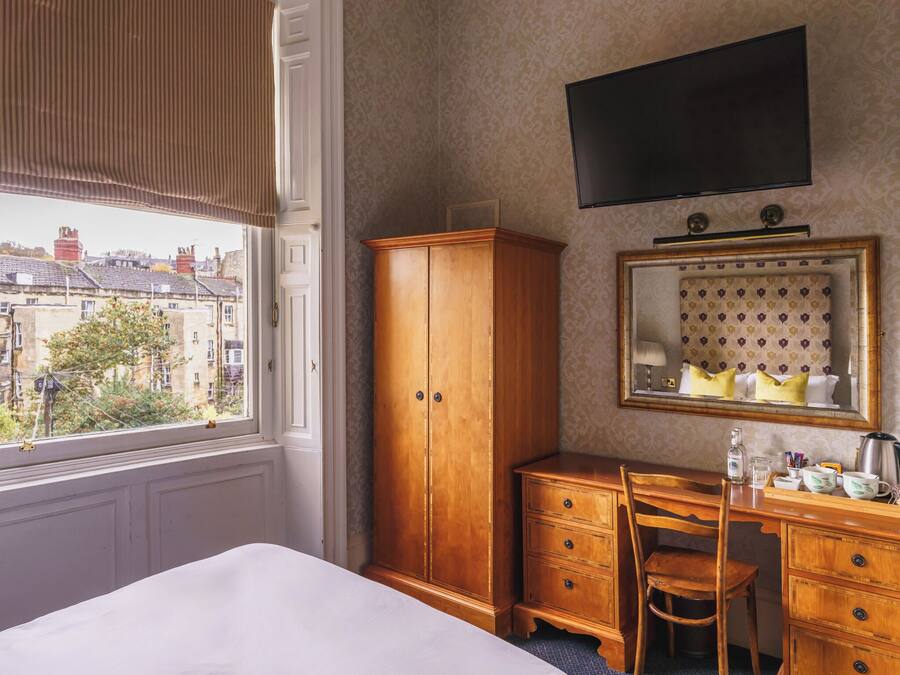 Ein Hotelzimmer mit großem Kleiderschrank, Schreibtisch mit Stuhl, Spiegel und Wandfernseher.