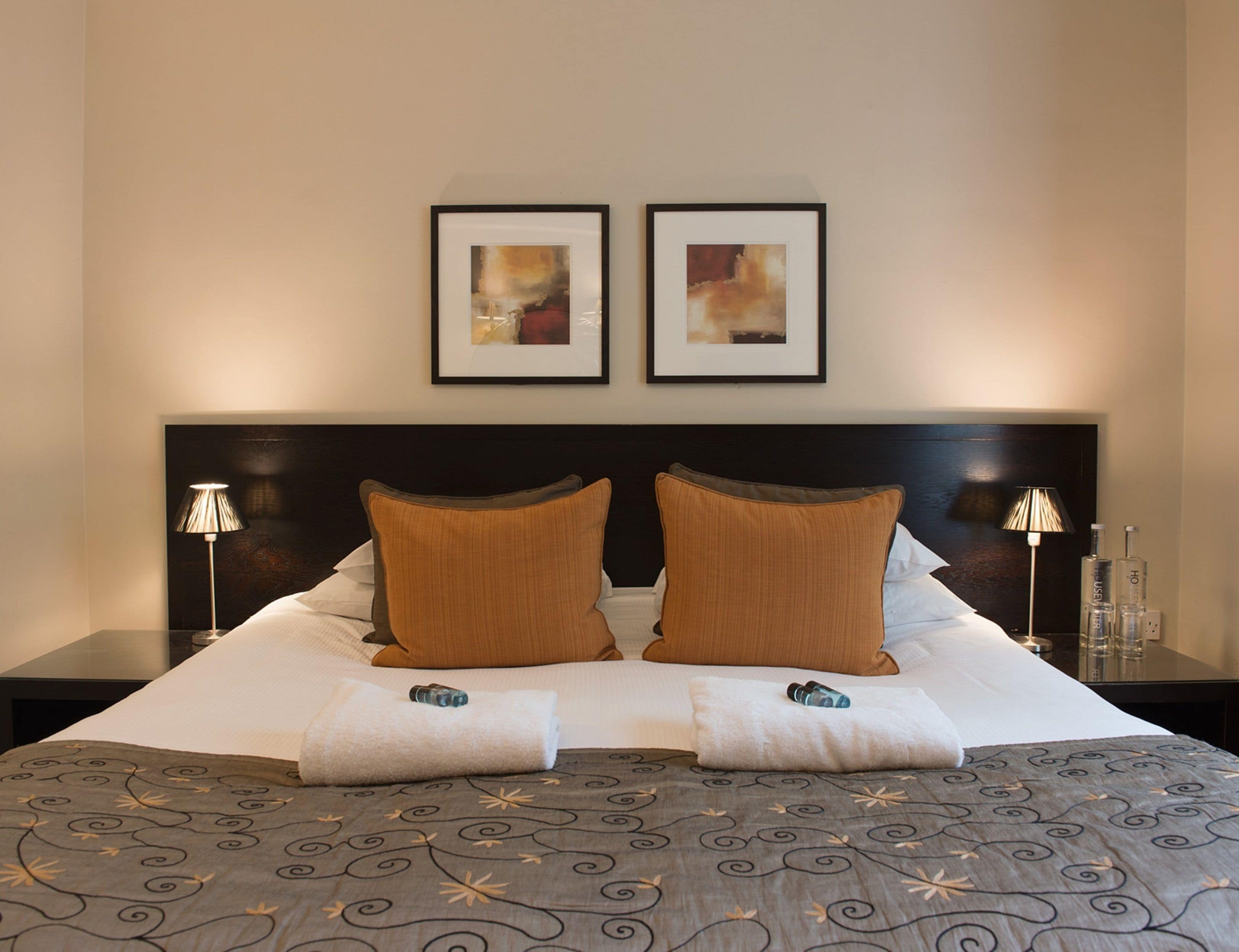 A neatly made bed with a patterned bedspread, two pillows, and a pair of framed artworks above it.