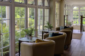 Una habitación amplia con ventanas grandes, varias zonas de estar y plantas en macetas.