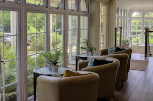 A spacious room with large windows, multiple seating areas, and potted plants.