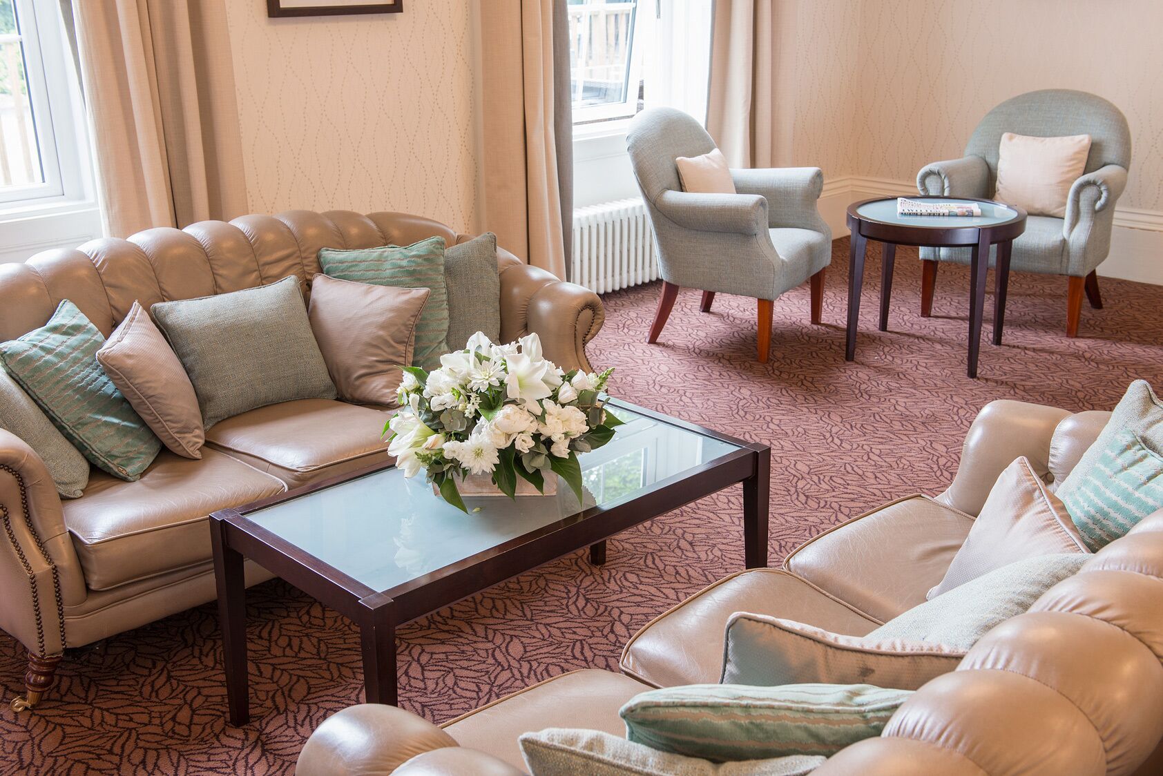 Una sala de estar bien amoblada con un sofá de cuero color beige, una mesa de centro de vidrio con un arreglo floral y dos sillones.