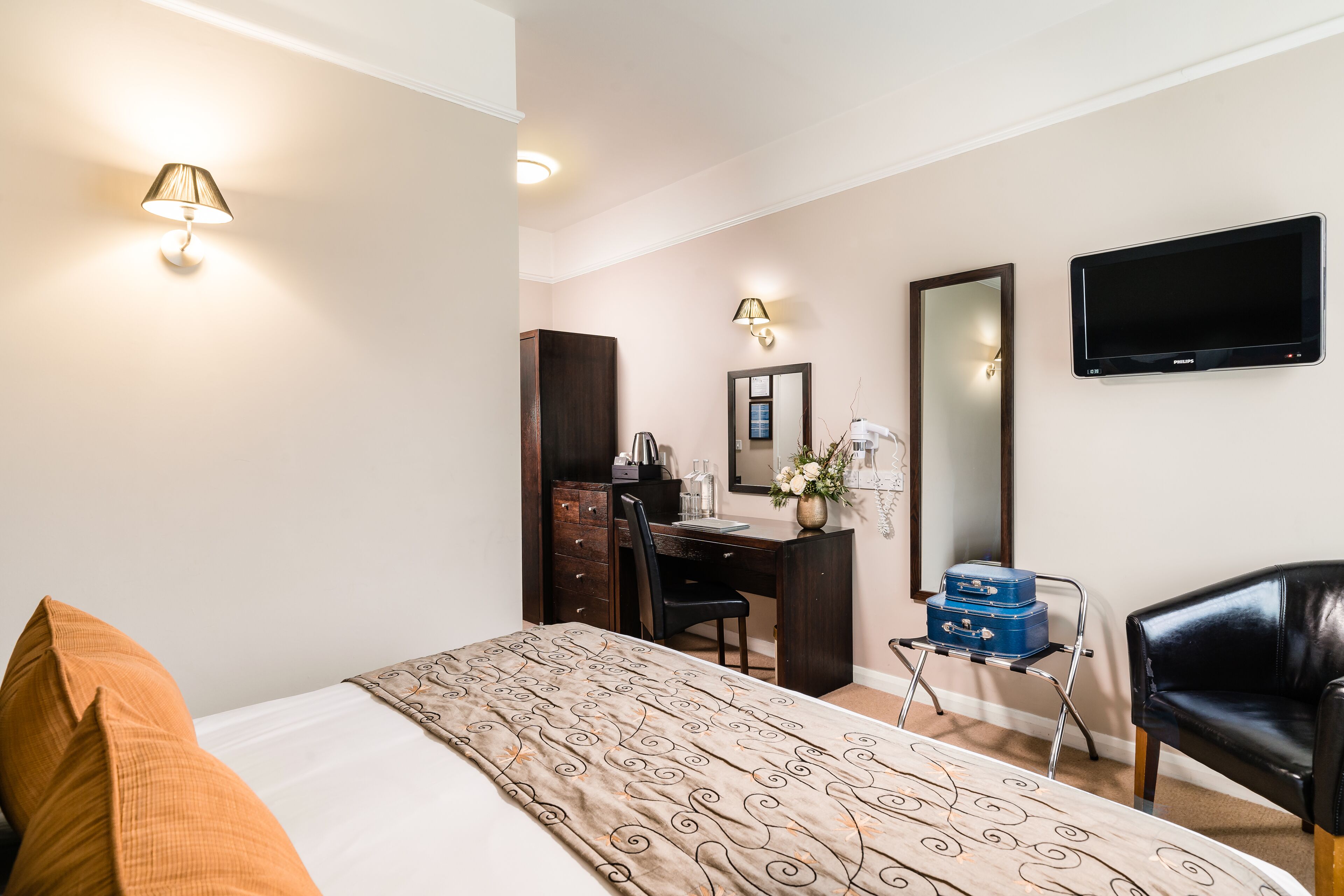 Quarto de hotel com cama, escrivaninha, cadeira, televisão e espelho.
