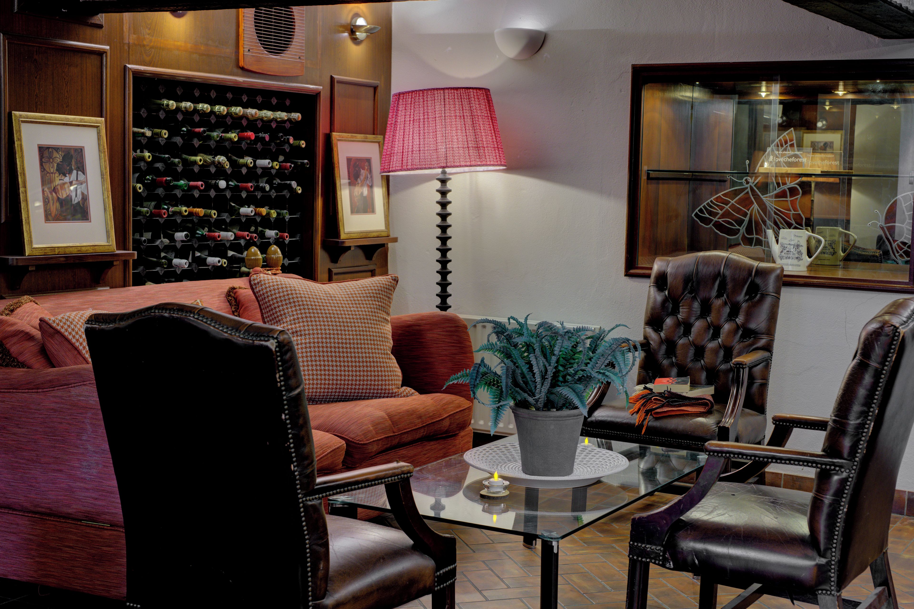 A cozy living room with a sofa, armchairs, a glass coffee table, a potted plant, and a wine rack.