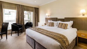 A hotel room with a large bed, two bedside tables, a chair, and a view of the outside. - Forest Lodge (Lyndhurst)