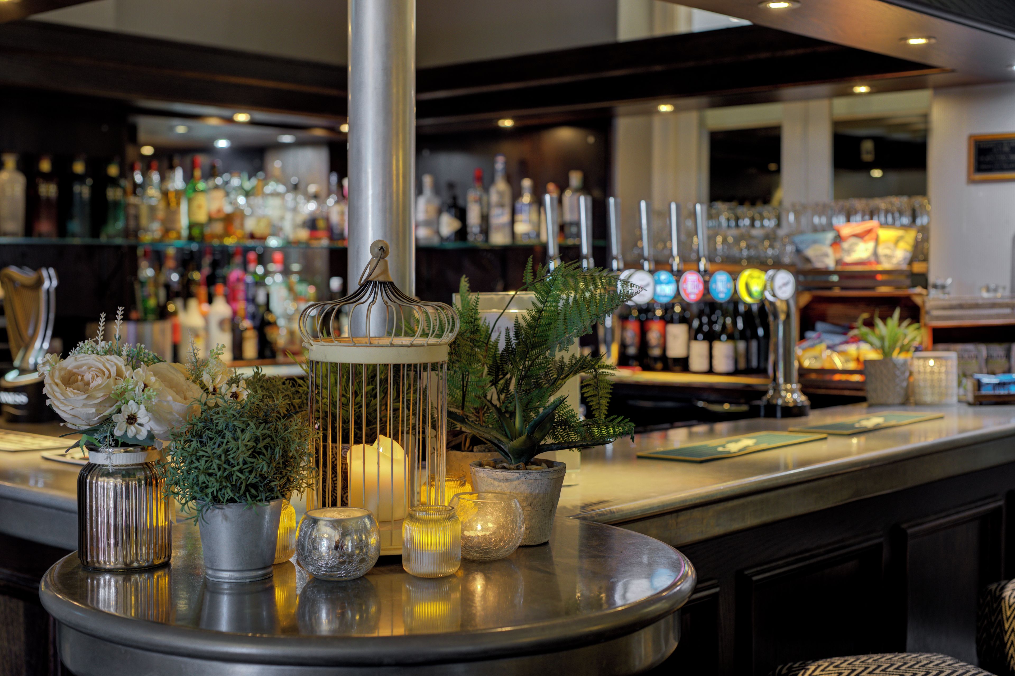 A bar area with a round table displaying various decorative items, including a candle, a plant, and a metal sculpture.