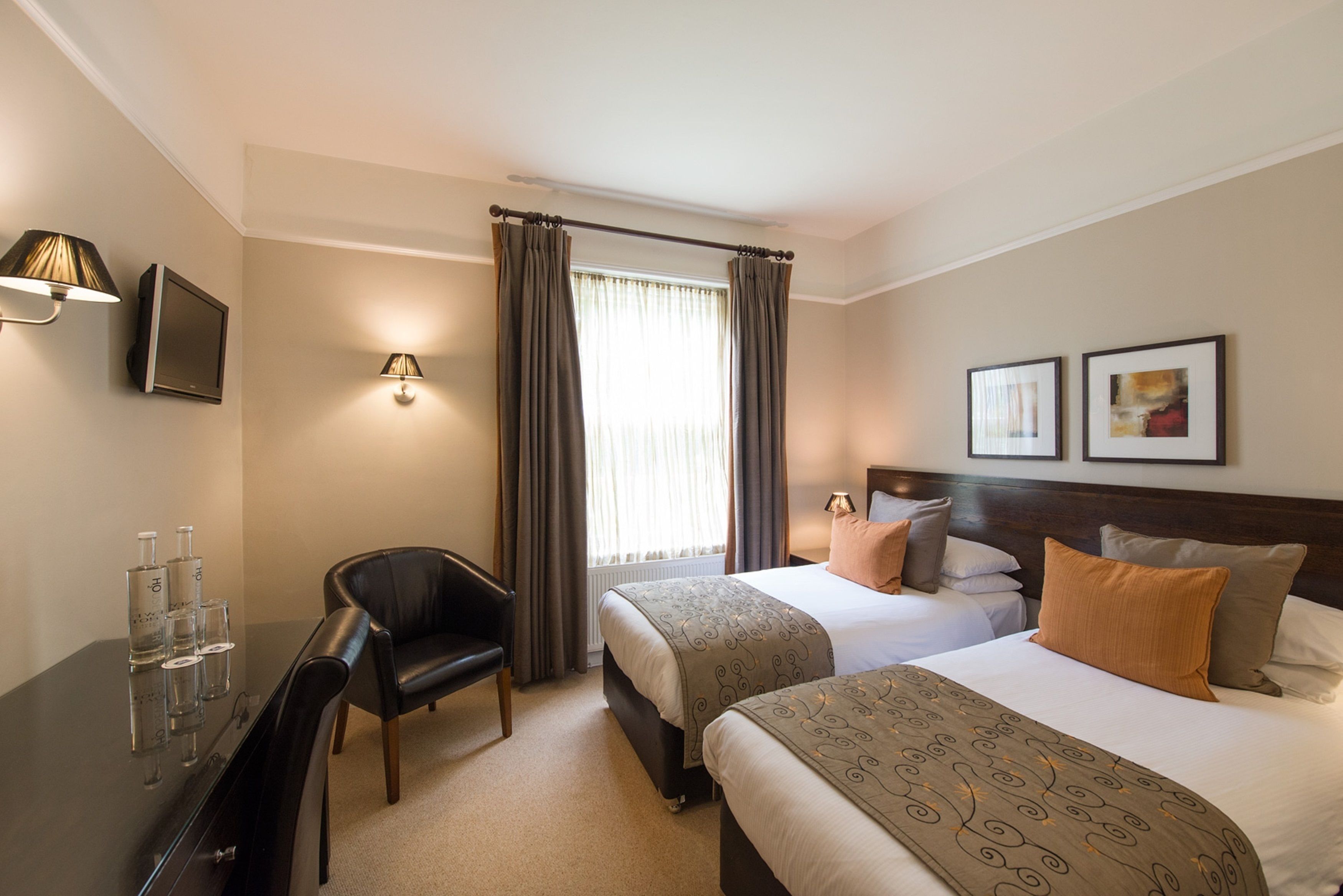 A hotel room with two beds, a desk with a chair, a TV, and a window with curtains.