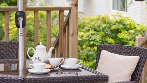 A wicker table set with white teapot, cups, and biscuits on a balcony with wooden railings and hanging flower baskets. - Forest Lodge (Lyndhurst)