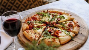 A pizza on a wooden board with a glass of red wine beside it. - Forest Lodge (Lyndhurst)
