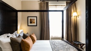 A hotel room with a large bed, a nightstand with a lamp, a framed picture on the wall, and a window with curtains. - Forest Lodge (Lyndhurst)
