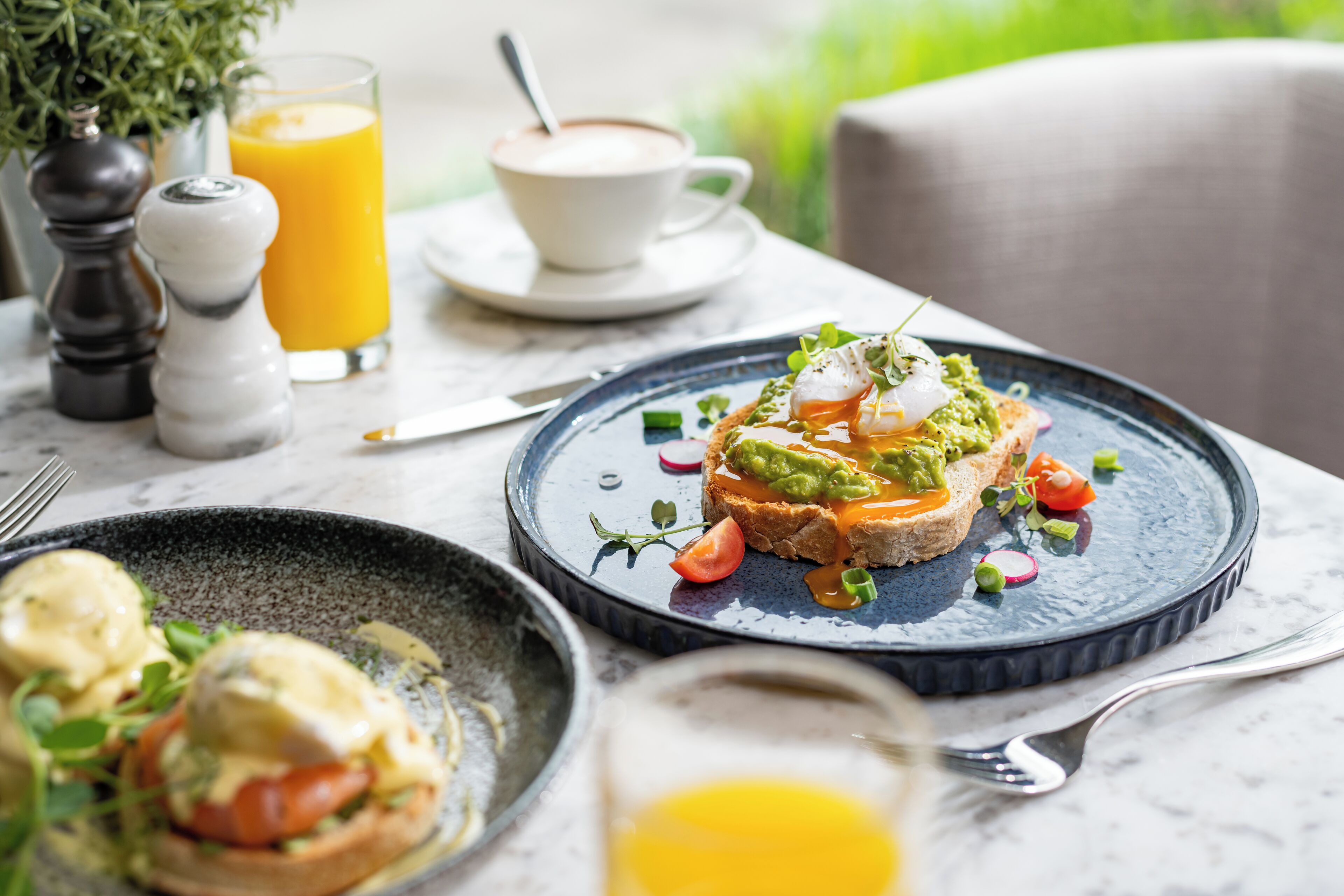A breakfast setting with a plate of toast topped with avocado and poached eggs, a glass of orange juice, and a cup of coffee.