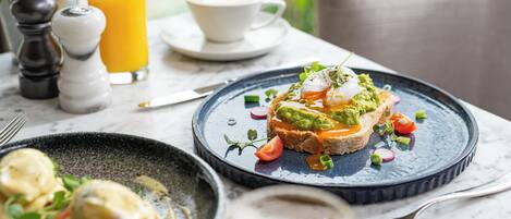 A breakfast setting with a plate of toast topped with avocado and poached eggs, a glass of orange juice, and a cup of coffee.