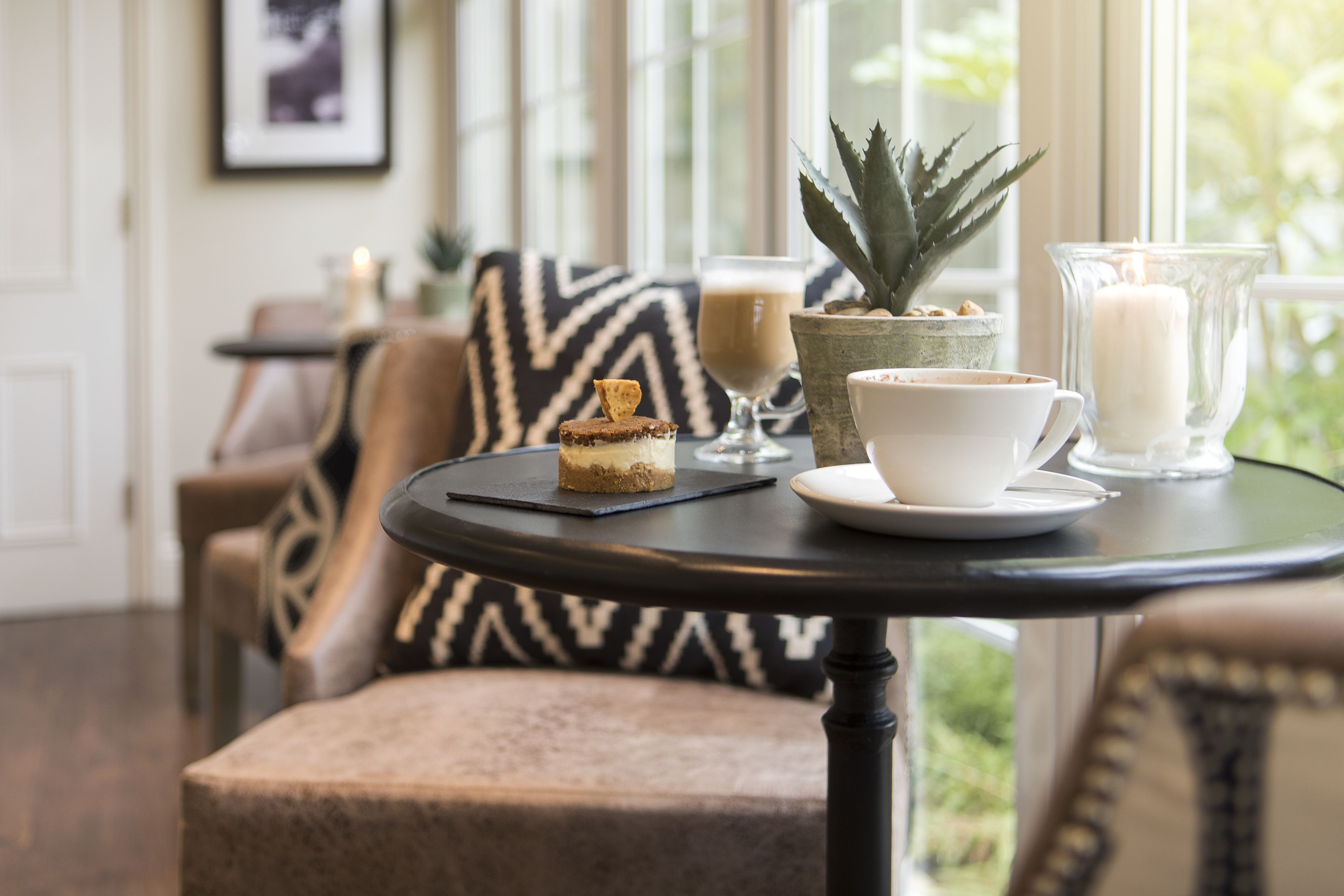 A cozy seating area with a round table, a dessert, a cup, and a candle.
