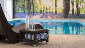 A poolside area with a wicker lounge chair, a glass table with bottles and towels, and a mural of a forest scene. - Forest Lodge (Lyndhurst)