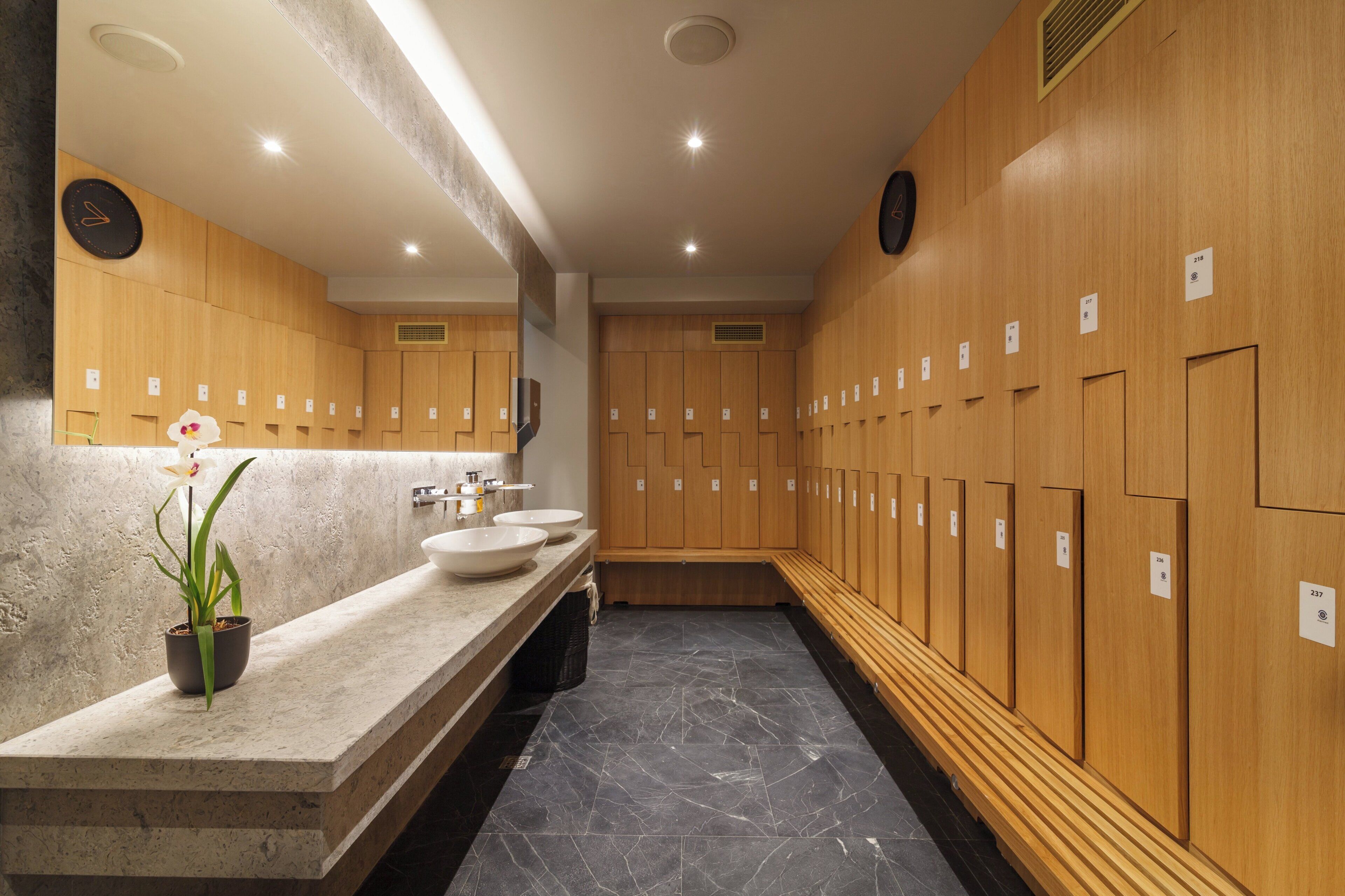 Une salle de bain moderne avec des casiers en bois, des vasques en marbre et une orchidée en pot.