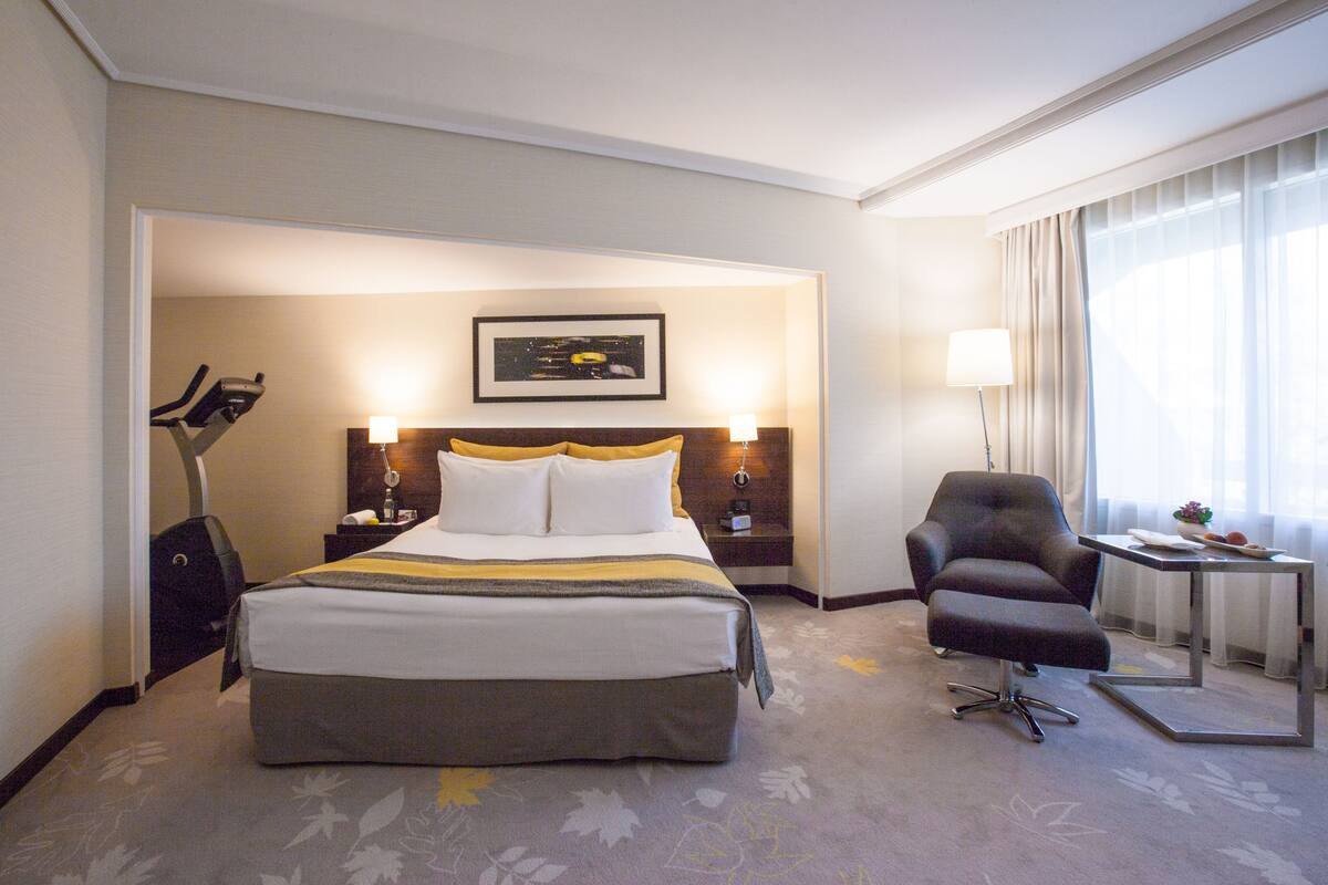 Ein Hotelzimmer mit einem großen Bett, einem Schreibtisch, einem Stuhl, einer Lampe und einem Bild an der Wand.