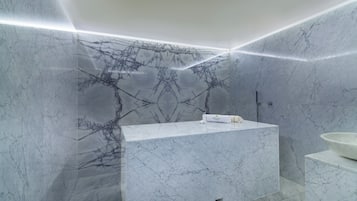 Casa de banho moderna com toucador de mármore, zona de duche e lavatório com divisória de vidro.