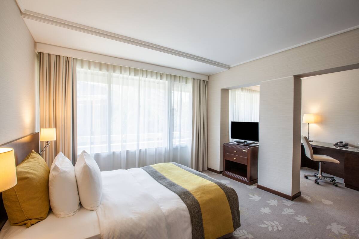 Ein Hotelzimmer mit Bett, Schreibtisch, Stuhl, Fernseher und Lampe.