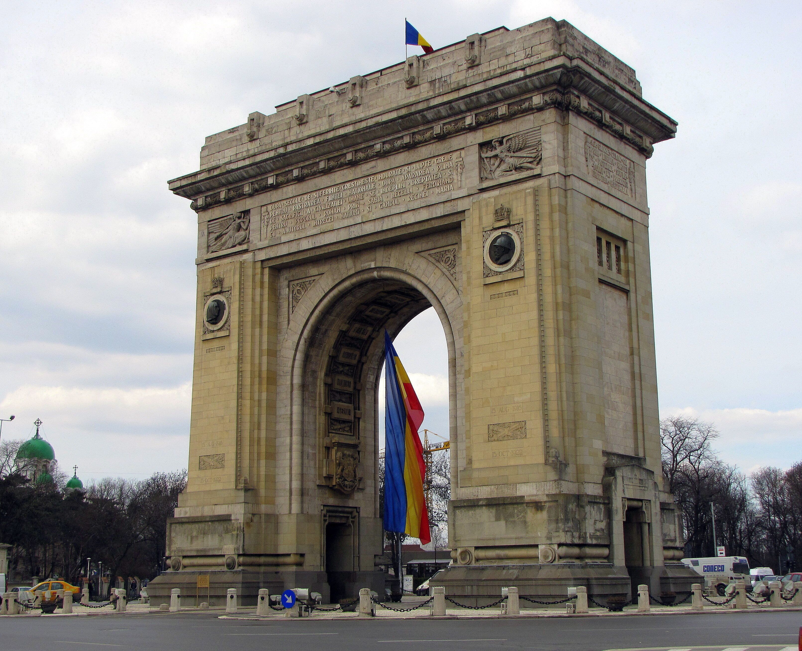 A large stone arch monument with inscriptions and a flag.