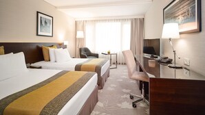 A hotel room with two beds, a desk with a chair, a TV, and a lamp. - Crowne Plaza Bucharest by IHG (Bucharest)