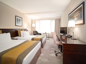 A hotel room with two beds, a desk with a chair, a TV, and a lamp.