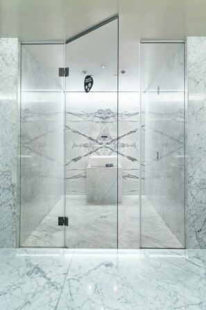 Un baño moderno con paredes de mármol y un lavamanos central.
