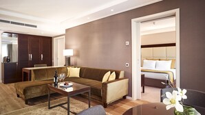 A modern hotel room with a brown sofa, a dining table, a small coffee table, and a separate seating area with a chair. - Crowne Plaza Bucharest by IHG (Bucharest)