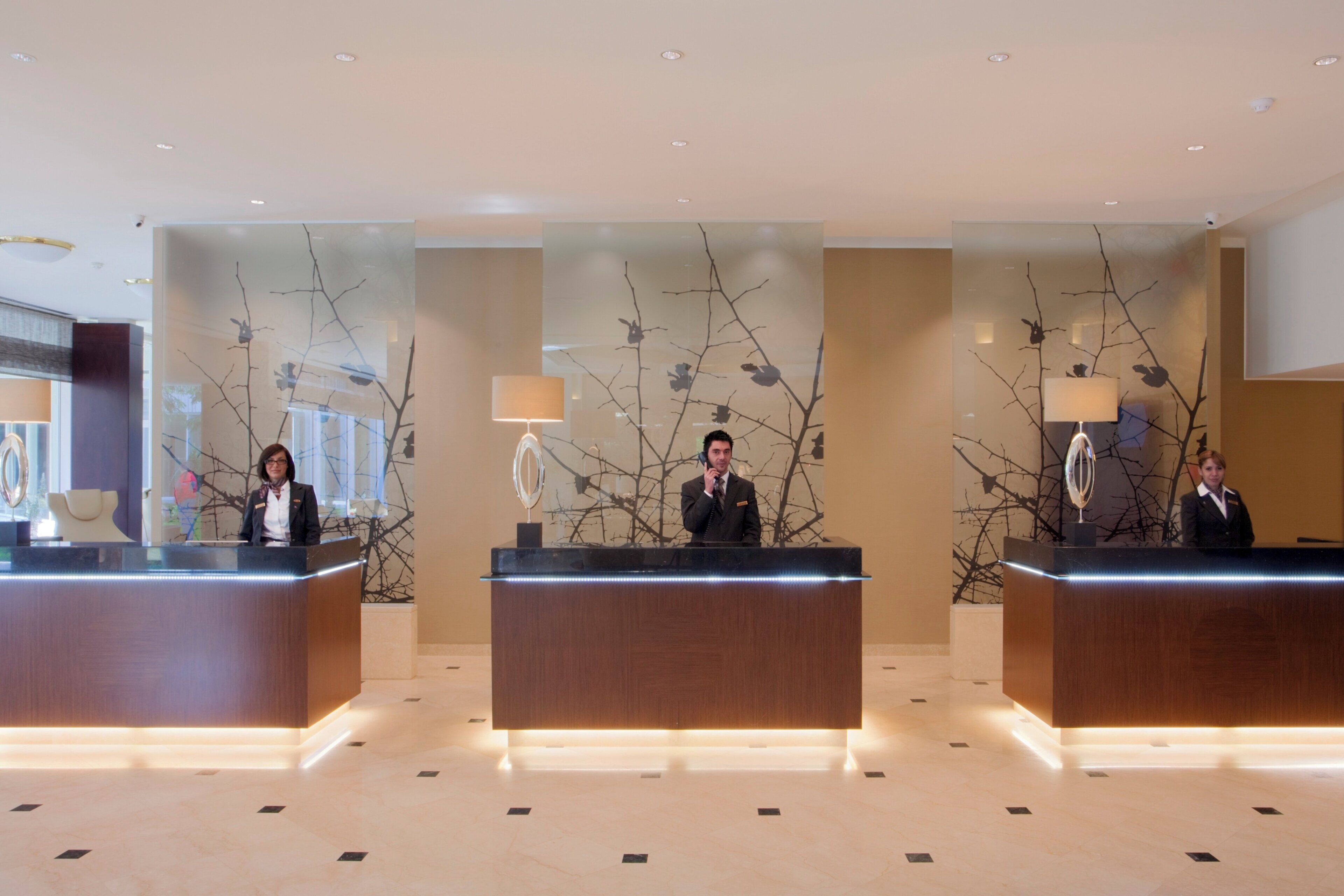 A hotel reception area with three receptionists at their desks, each with a lamp and a telephone.