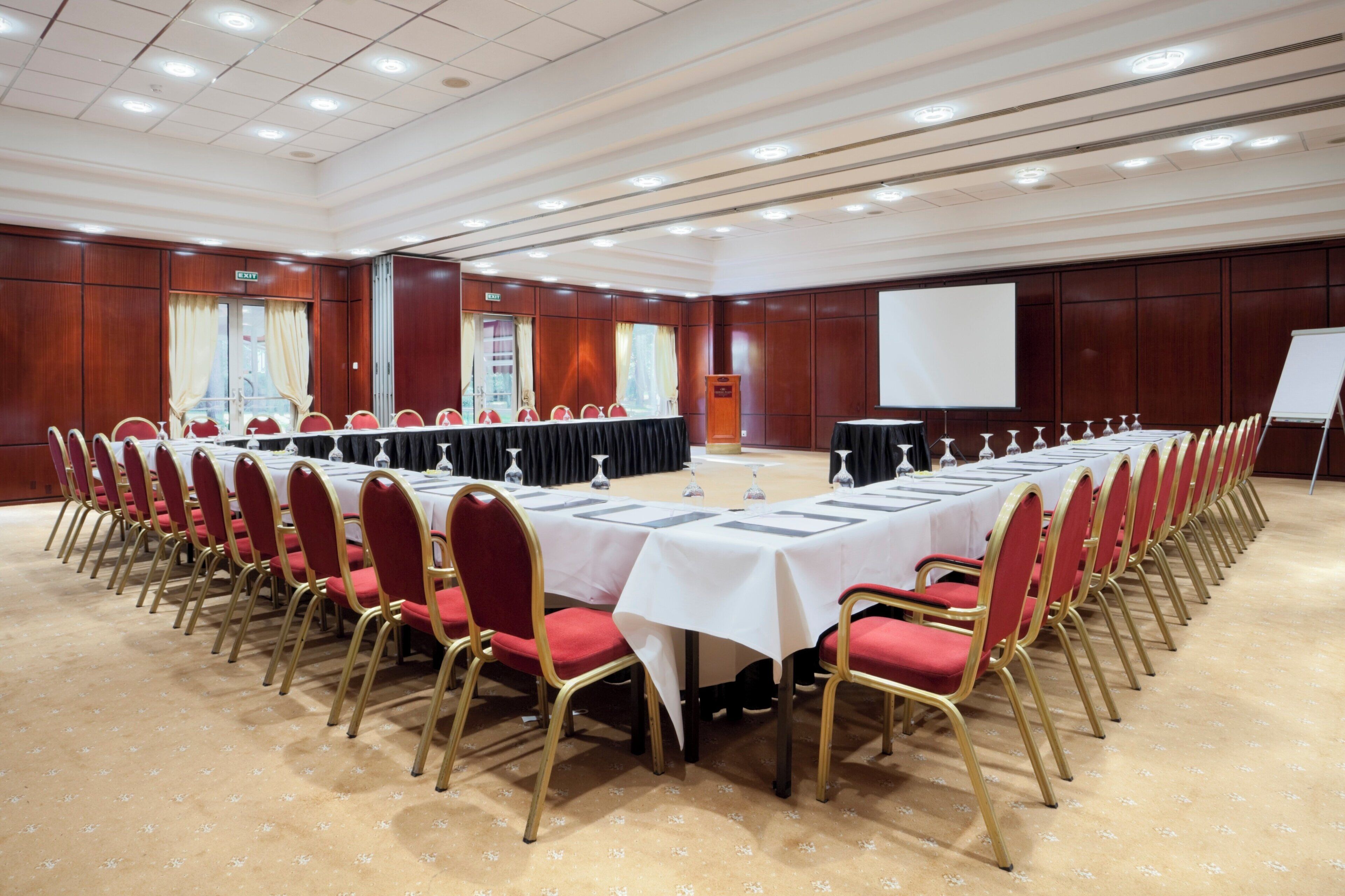 A conference room with a long table, red chairs, and a projector screen.