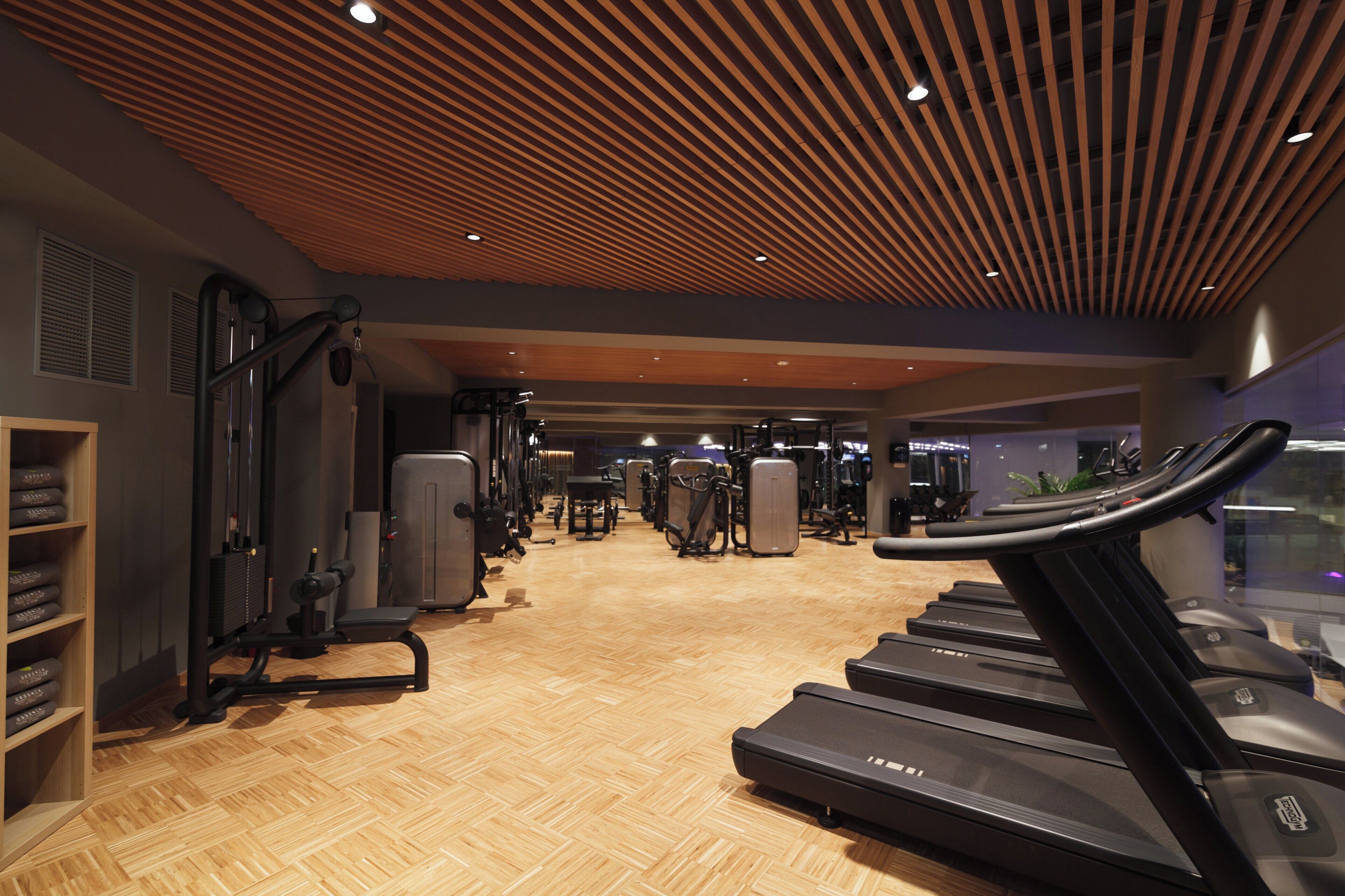 Ein Fitnessstudio mit Laufbändern, Krafttrainingsgeräten und Holzboden.