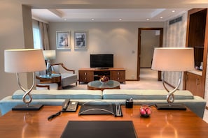 A modern hotel room with a sofa set, a television, a coffee table, and two lamps.