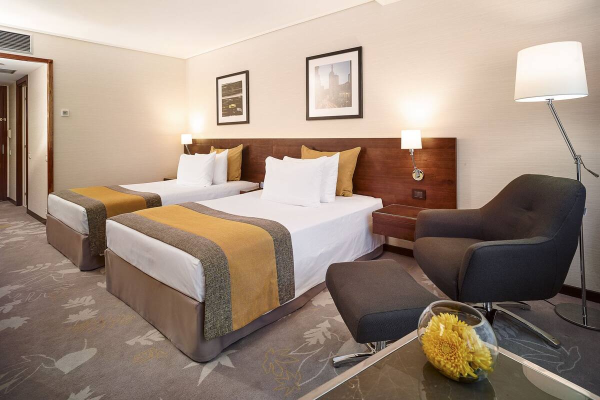Ein Hotelzimmer mit zwei Betten, einem Schreibtisch, einem Stuhl und einer Lampe.