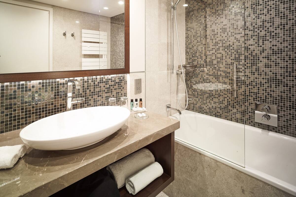 Ein modernes Badezimmer mit einem großen Waschbecken, einer Duschkabine und einer mosaikverzierten Wand.