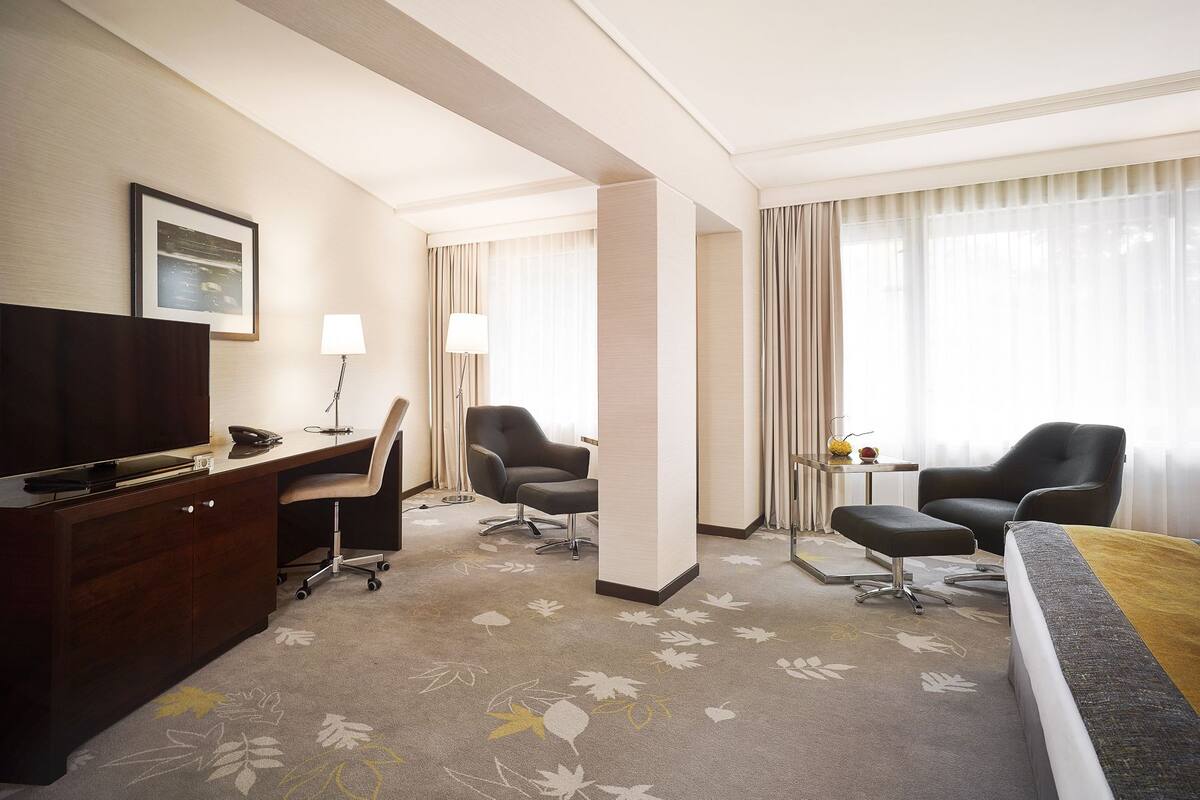 Ein Hotelzimmer mit Schreibtisch, zwei Sesseln, einem Fernseher und einem Bett.