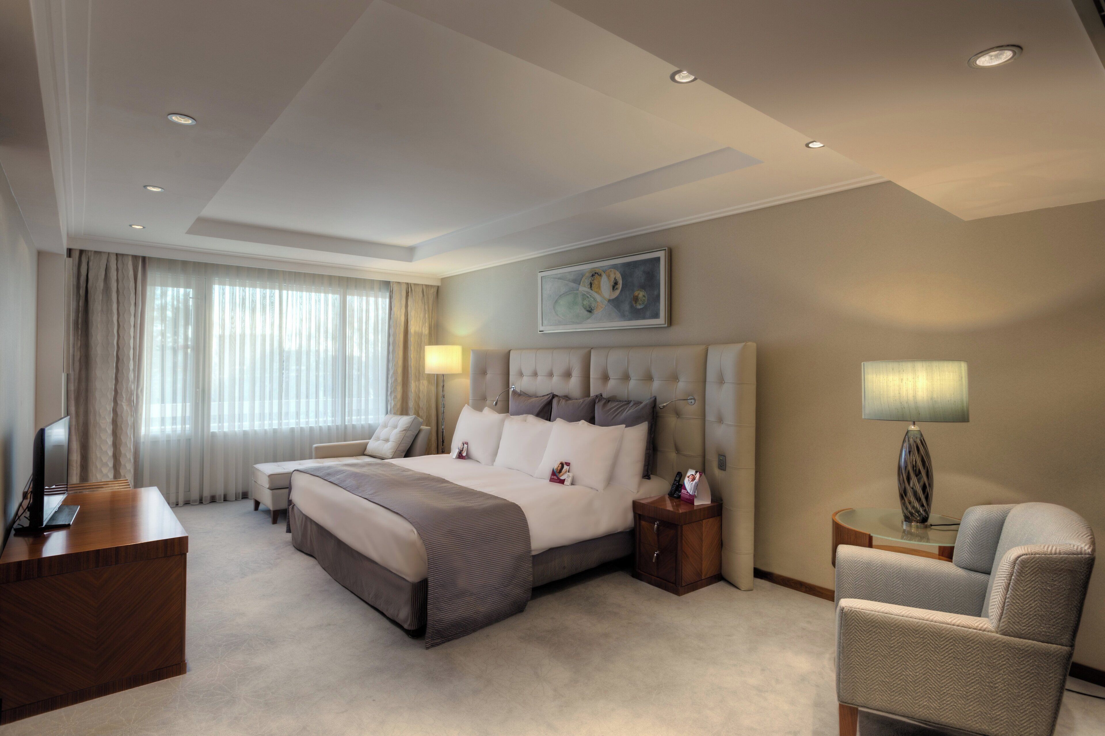 A hotel room with a large bed, bedside tables, a chair, and a desk.
