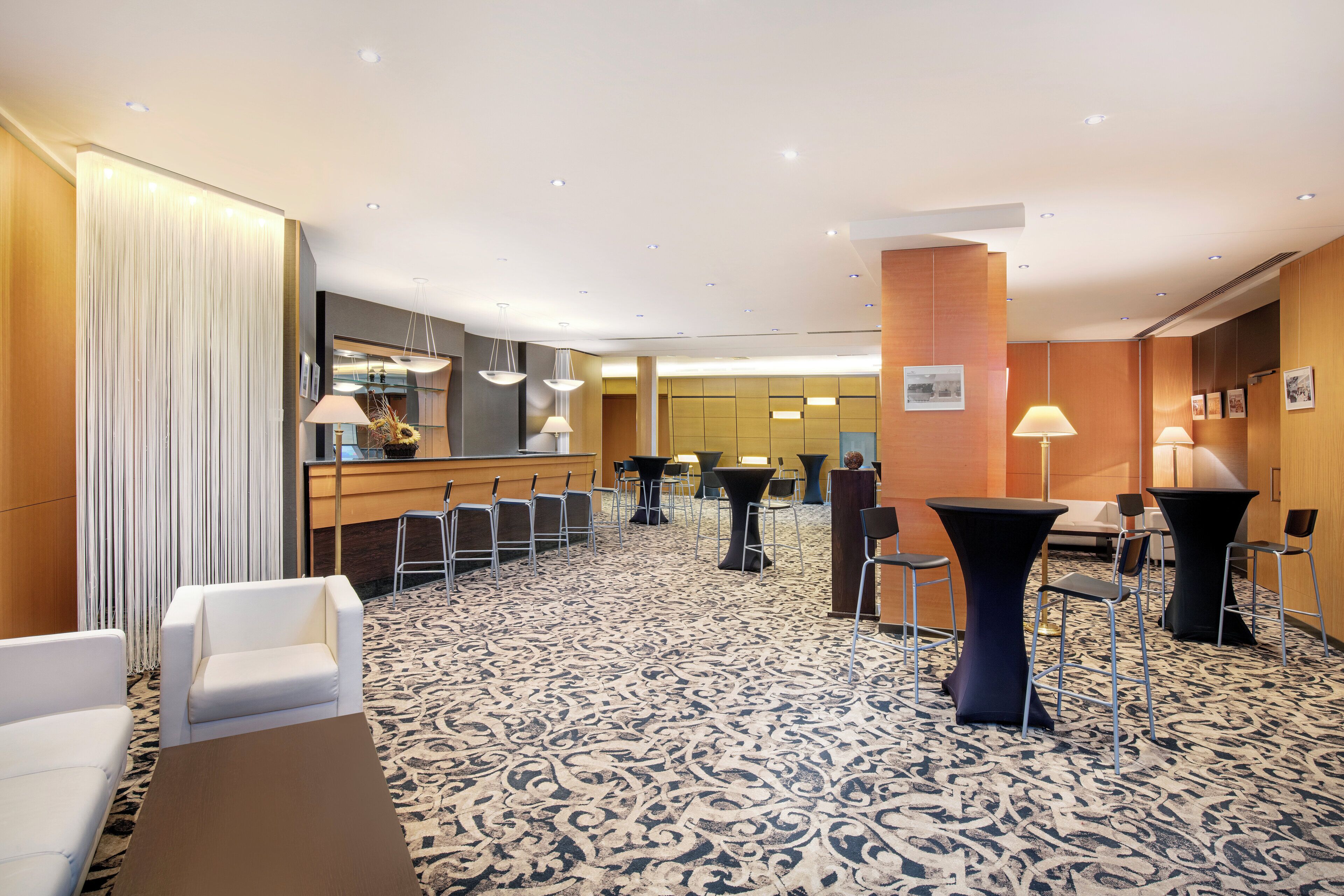 Et hotel lobby med receptionsdisk, siddeområde og et mønstret tæppe.