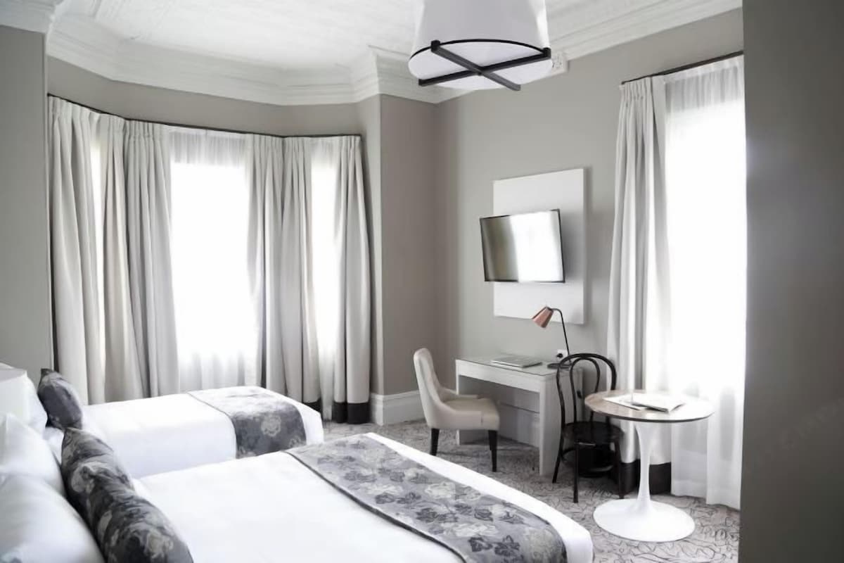 A hotel room with a large bed, a desk, a chair, and a small table.