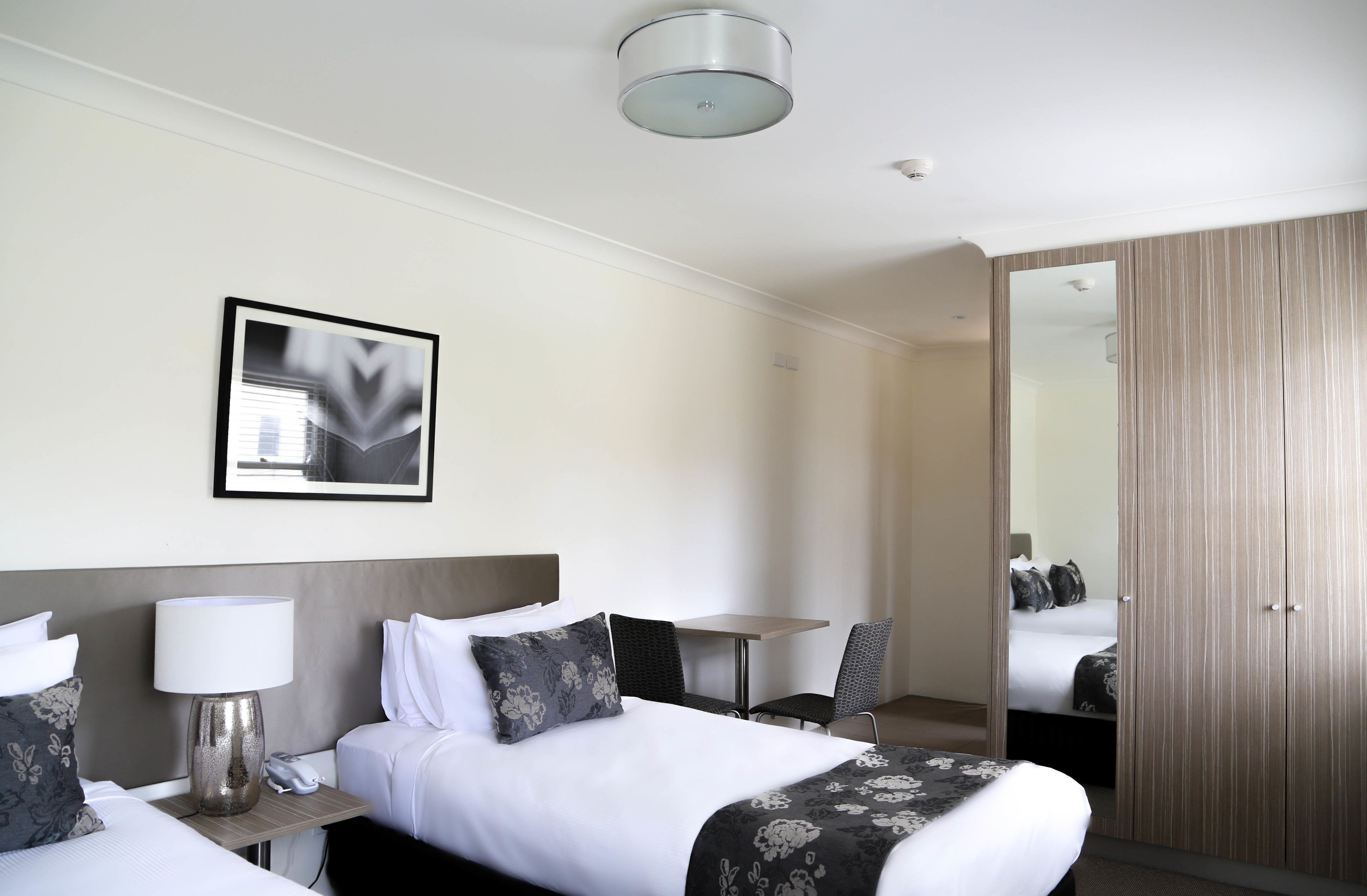 Habitación de hotel con cama, mesita de noche, lámpara, silla y espejo.