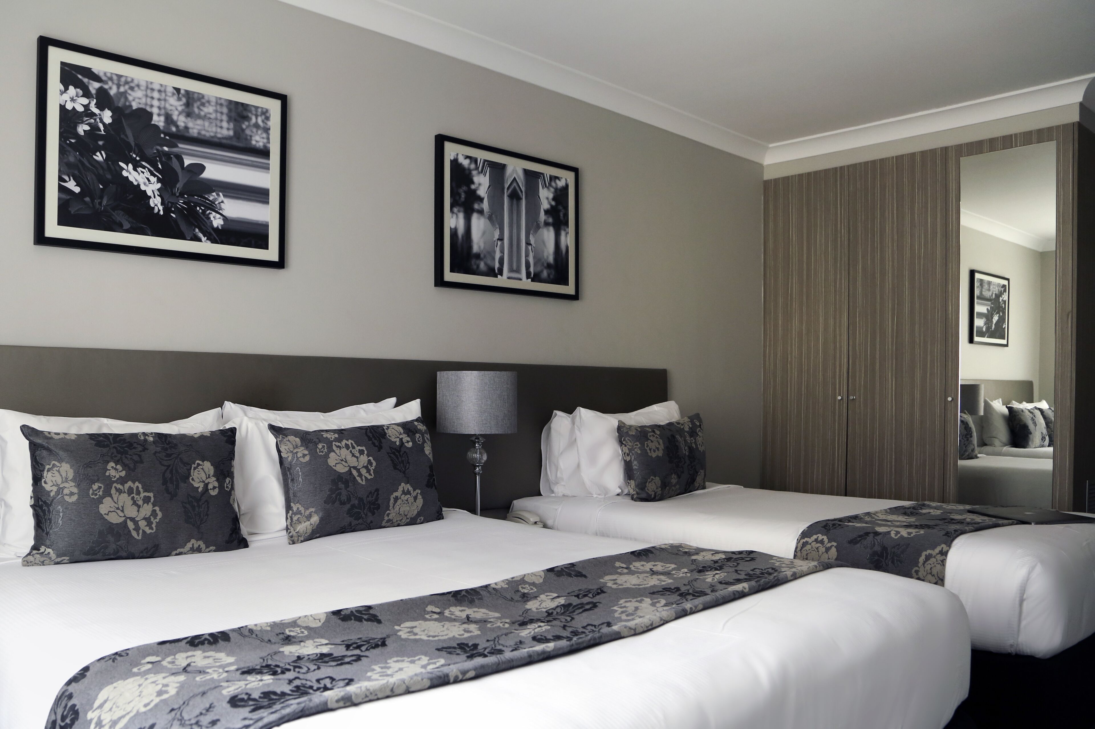 A hotel room with two beds, a large mirror, and two framed pictures on the wall.
