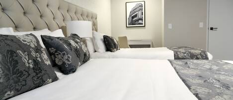 A hotel room with a tufted headboard, a large bed with floral-patterned bedding, a bedside table with a lamp, and a framed picture on the wall.