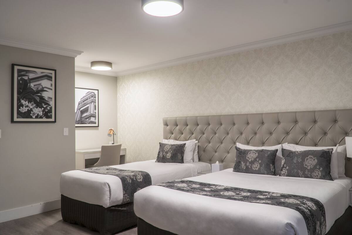 A hotel room with two beds, a tufted headboard, and a small desk with a lamp.