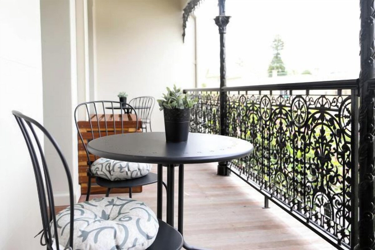 A balcony with a round table and two chairs, a potted plant, and a decorative railing.