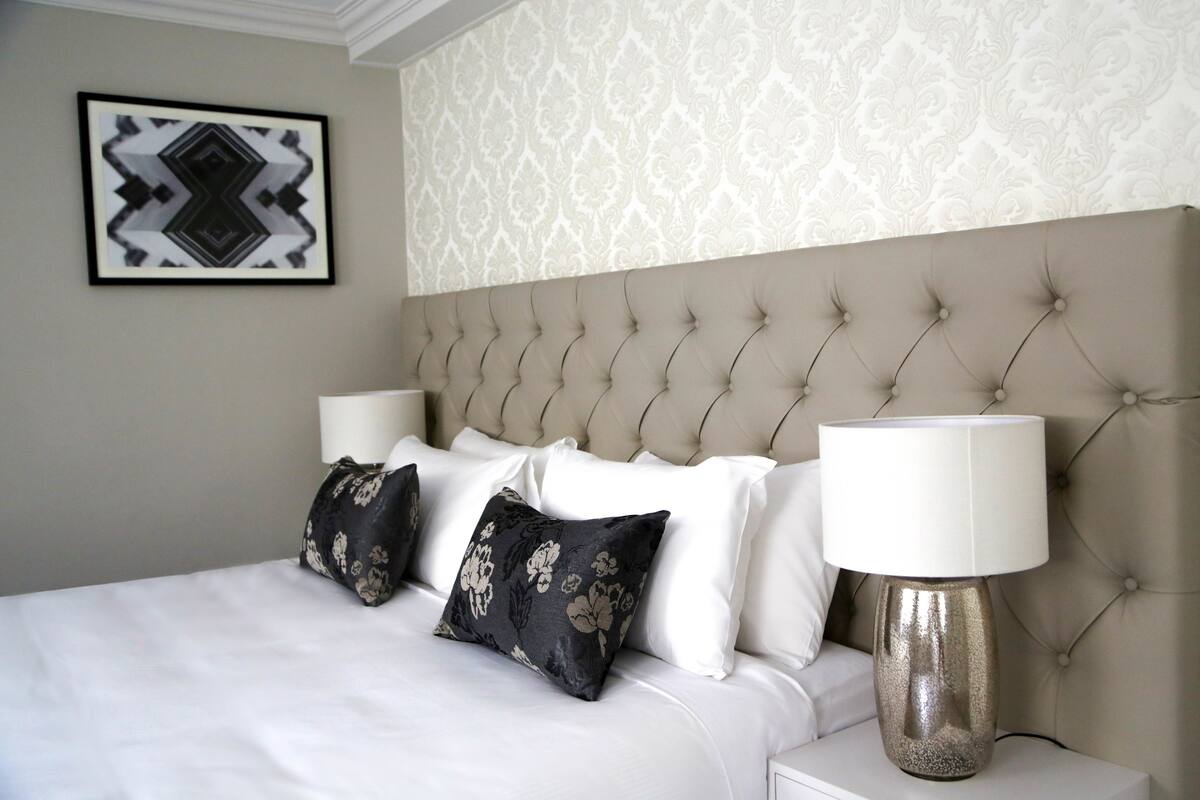 A neatly made bed with a tufted headboard, two bedside lamps, and a floral-patterned pillow.