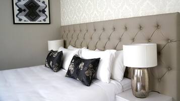 A neatly made bed with a tufted headboard, two bedside lamps, and a floral-patterned pillow.