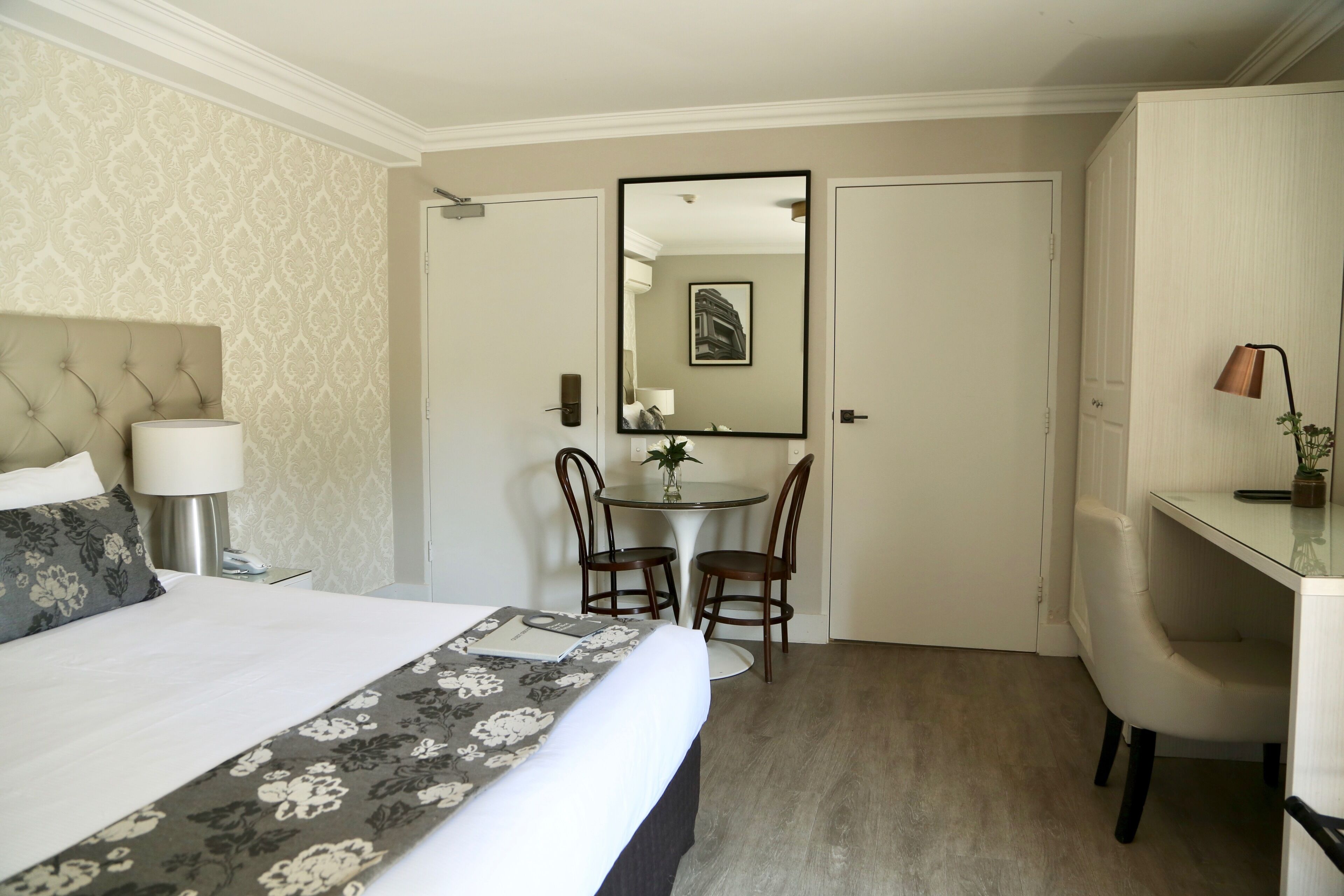 A hotel room with a bed, a desk, a chair, a round table, and a mirror.