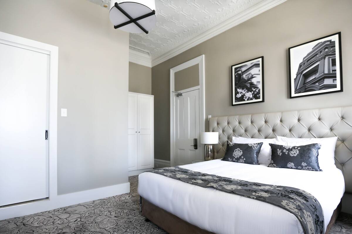 A hotel room with a large bed, a tufted headboard, and two framed pictures on the wall.